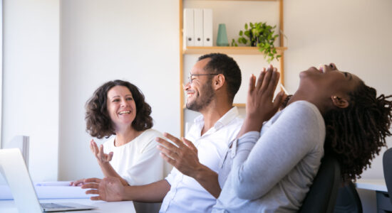 Cheerful employees talking and laughing at workplace. Group of smiling workers having fun in office. Teamwork and relaxation concept